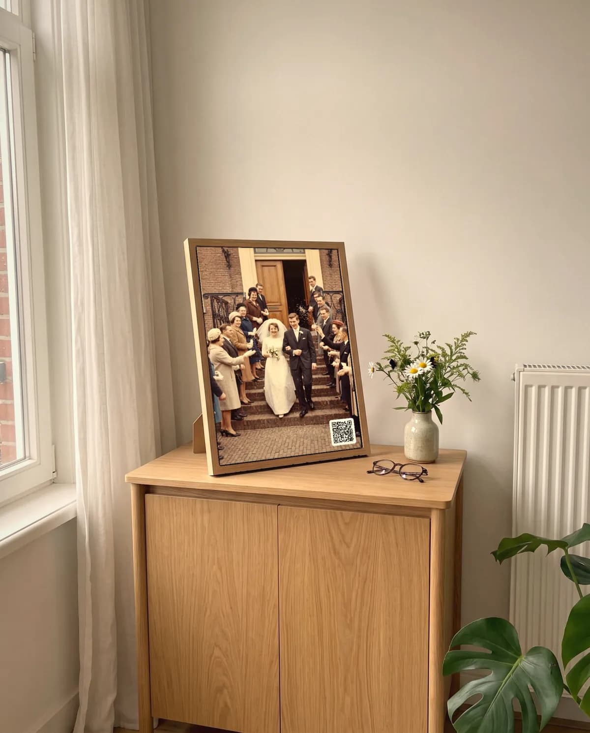 Een Verhaallijst met een trouwfoto uit 1962 en een QR-code in de hoek op een eiken kastje in een lichte woonkamer